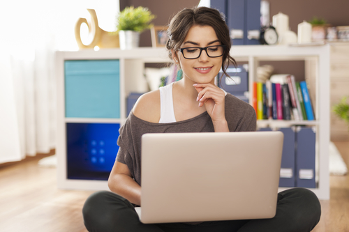 Smiling woman using laptop on floor at home