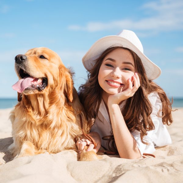 Portrait of cheerful beautiful young woman lying with her dog on the beach